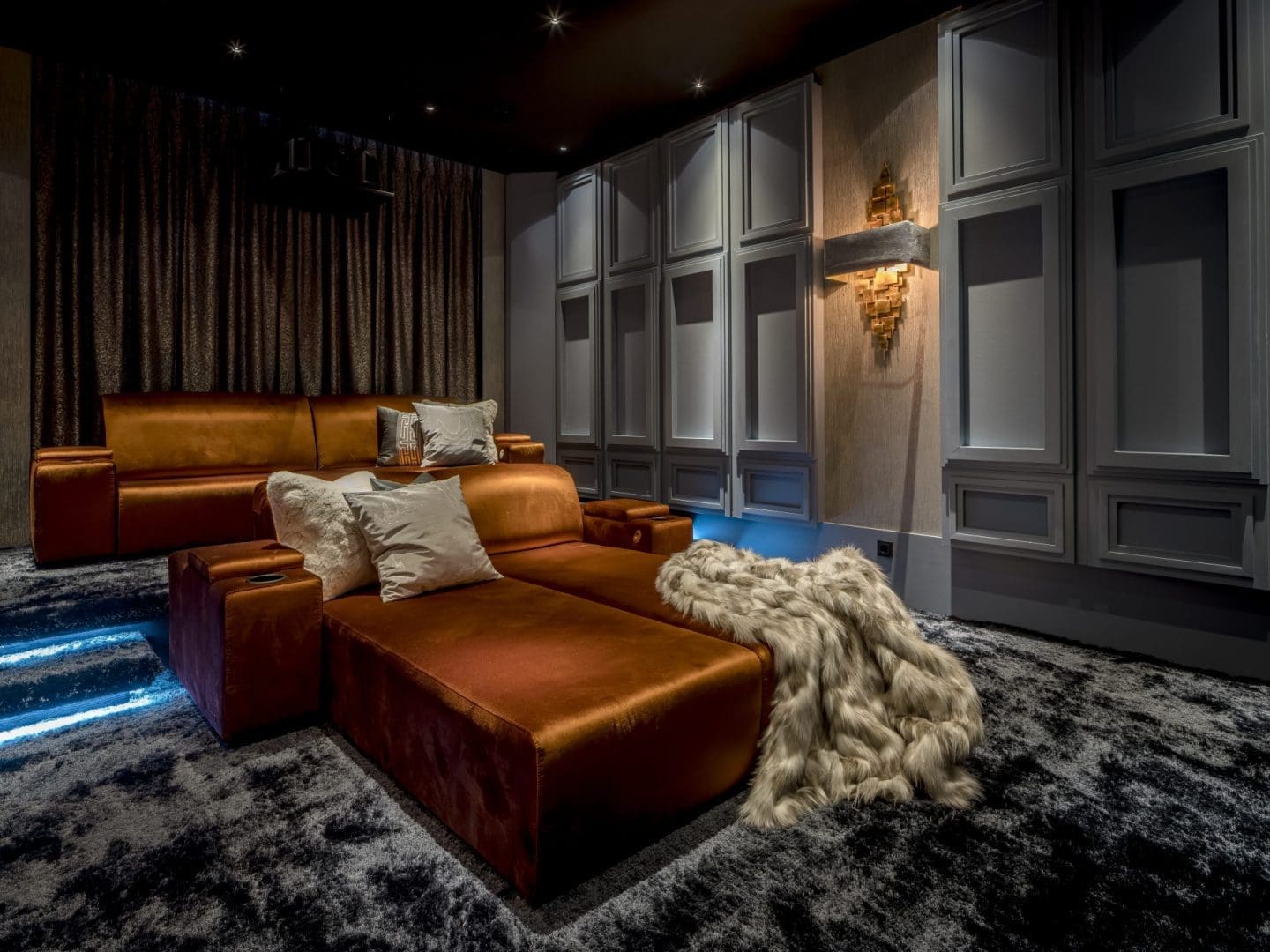 Luxe thuisbioscoop met koperkleurige fluwelen banken, een pluizige deken en sfeervolle wandverlichting in Project Solis. Luxe thuisbioscoop met koperkleurige fluwelen banken, een pluizige deken en sfeervolle wandverlichting in Project Solis.