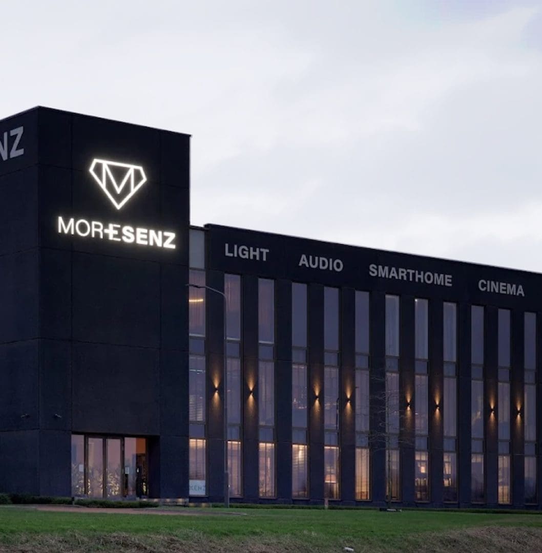 Modern zwart bedrijfspand met verlichte Moresenz-logo en teksten voor Light, Audio, Smarthome en Cinema. Modern zwart bedrijfspand met verlichte Moresenz-logo en teksten voor Light, Audio, Smarthome en Cinema.