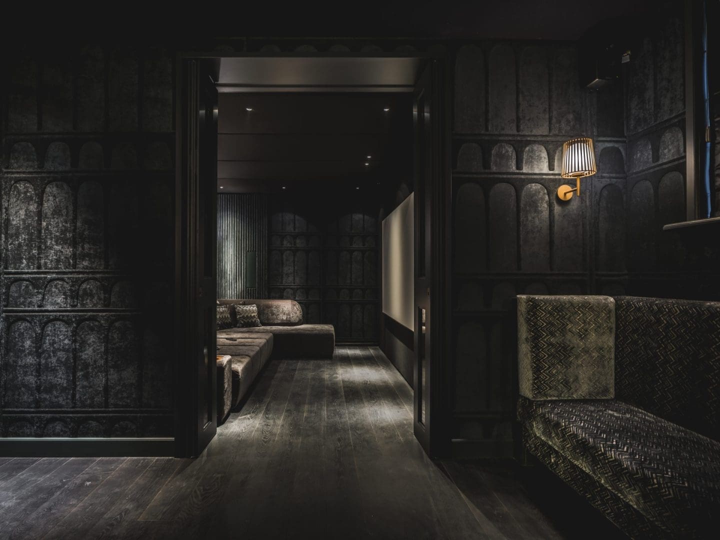Luxe, donker interieur met een bank en sfeervolle wandlamp in een kamer die uitkijkt op een aangrenzende lounge, Project Verd