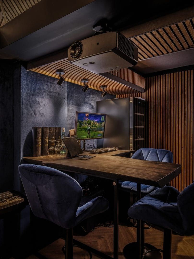 Houten bureau met blauwe stoelen, een computerscherm met een game, en een projector aan het plafond in een moderne kamer. Houten bureau met blauwe stoelen, een computerscherm met een game, en een projector aan het plafond in een moderne kamer.