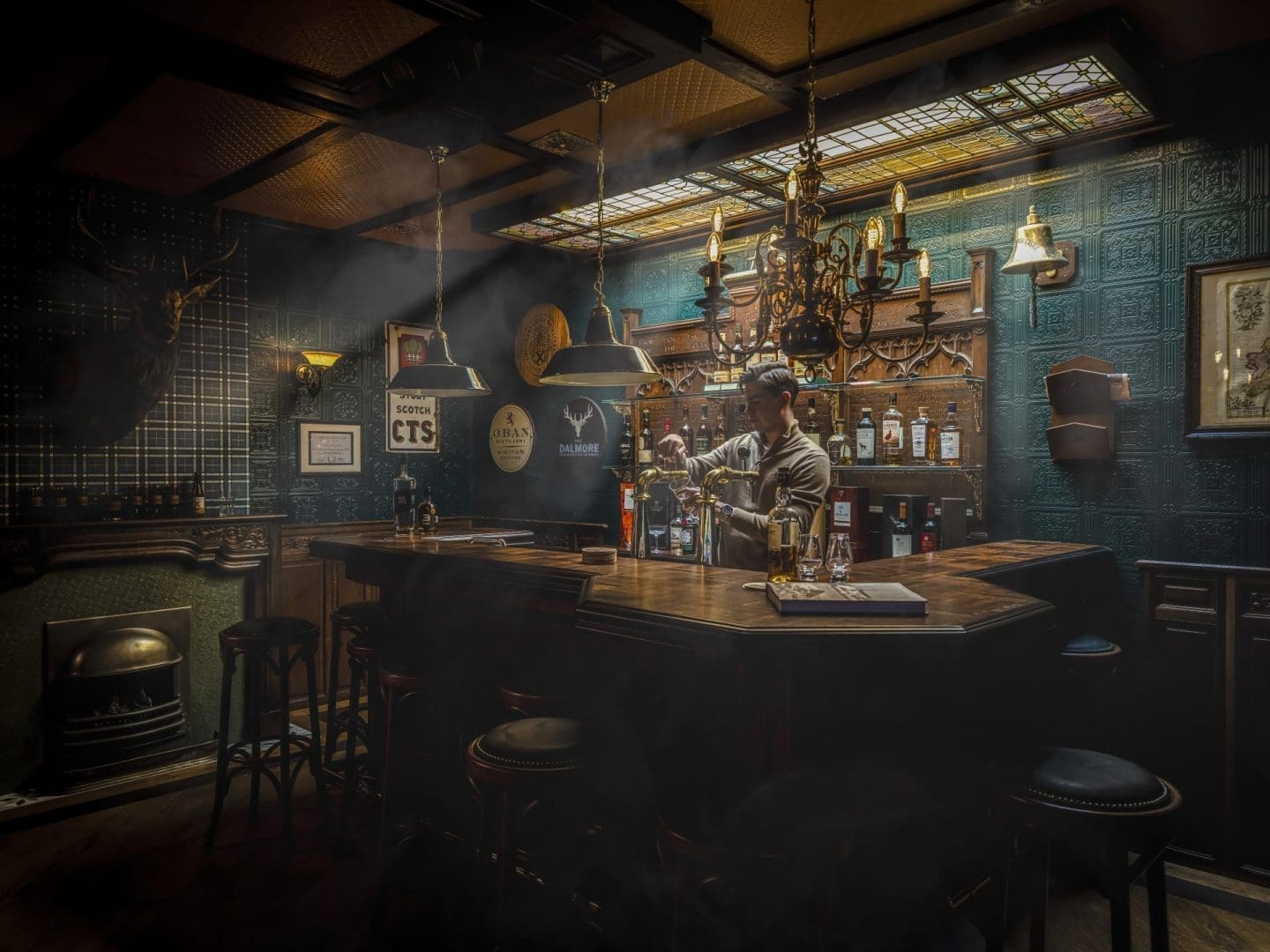 Barkeeper achter een houten bar in een sfeervolle pub met "CTS" en "Dalmore" logo's aan de muur. Barkeeper achter een houten bar in een sfeervolle pub met "CTS" en "Dalmore" logo's aan de muur.