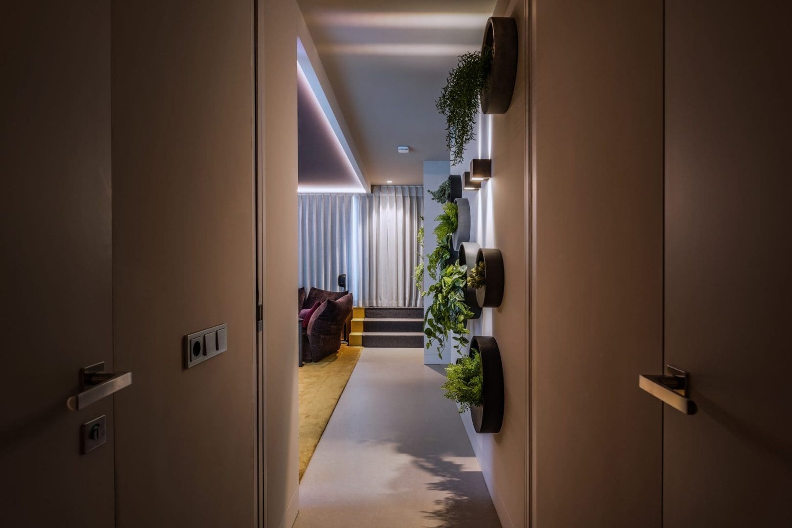 Een gang met ronde wandplantenbakken leidt naar een woonkamer met gordijnen en een bank in Project Oris 0.5. Een gang met ronde wandplantenbakken leidt naar een woonkamer met gordijnen en een bank in Project Oris 0.5.