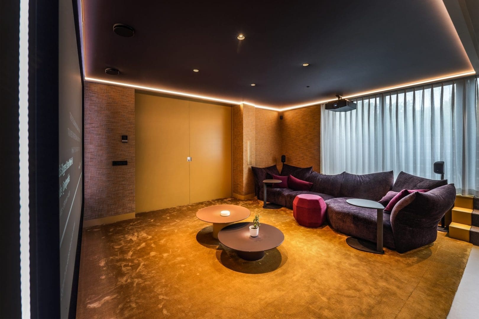 Een luxe thuisbioscoop met een paarse hoekbank, twee ronde salontafels, een geel tapijt en sfeervolle ledverlichting.