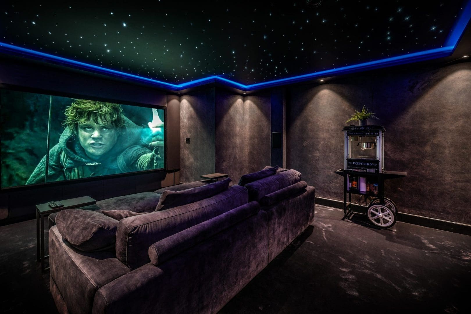 Thuisbioscoop met een grote bank, een sterrenhemelplafond en een popcornmachine, met Frodo op het scherm.