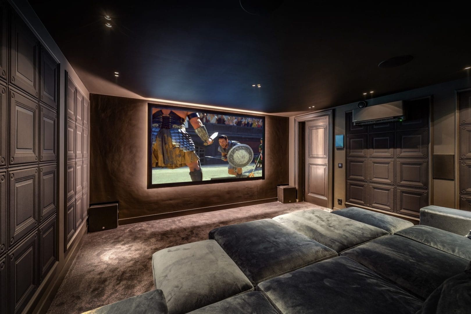 Luxe thuisbioscoop met een groot scherm waarop een filmscène te zien is, met comfortabele banken en donkere wandpanelen.