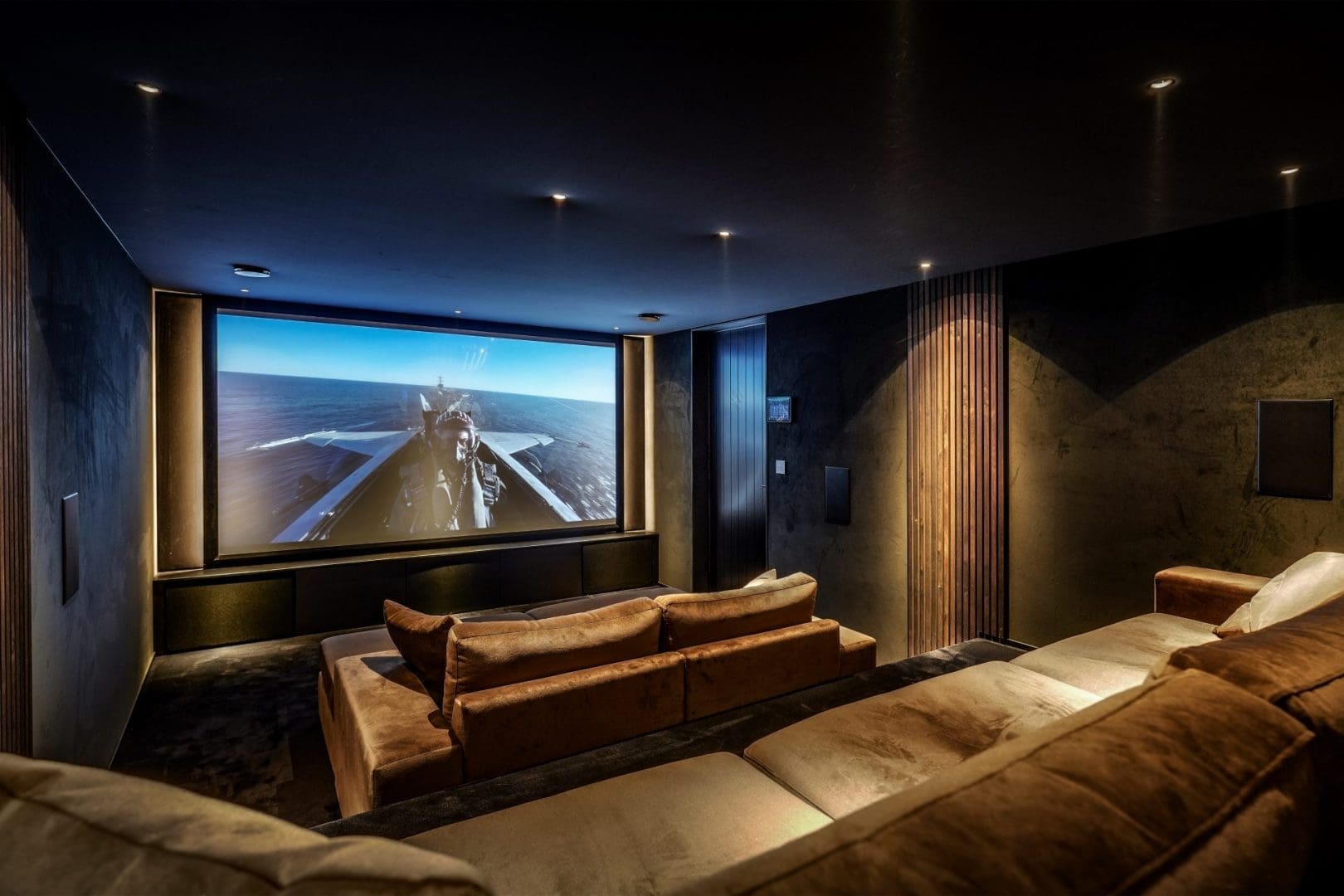 Luxe thuisbioscoop met bruine banken en een groot scherm waarop een straaljager boven zee te zien is, Project Oakmont 0.3.