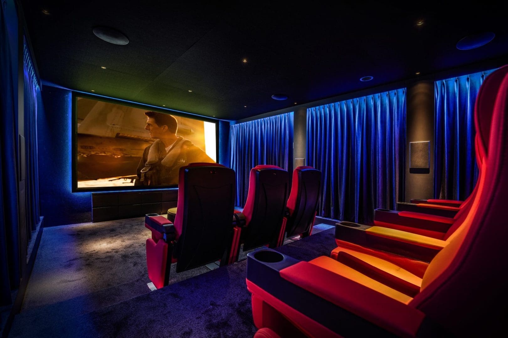 Luxe thuisbioscoop met rode fauteuils en een groot scherm waarop een filmscène van Project Scala 0.3 te zien is.