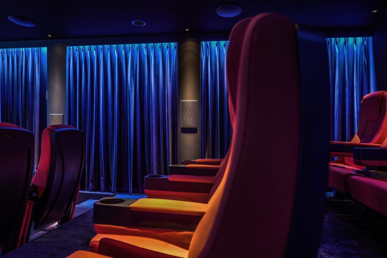 Rijen rode bioscoopstoelen in een donkere zaal met blauw verlichte gordijnen op de achtergrond. Rijen rode bioscoopstoelen in een donkere zaal met blauw verlichte gordijnen op de achtergrond.