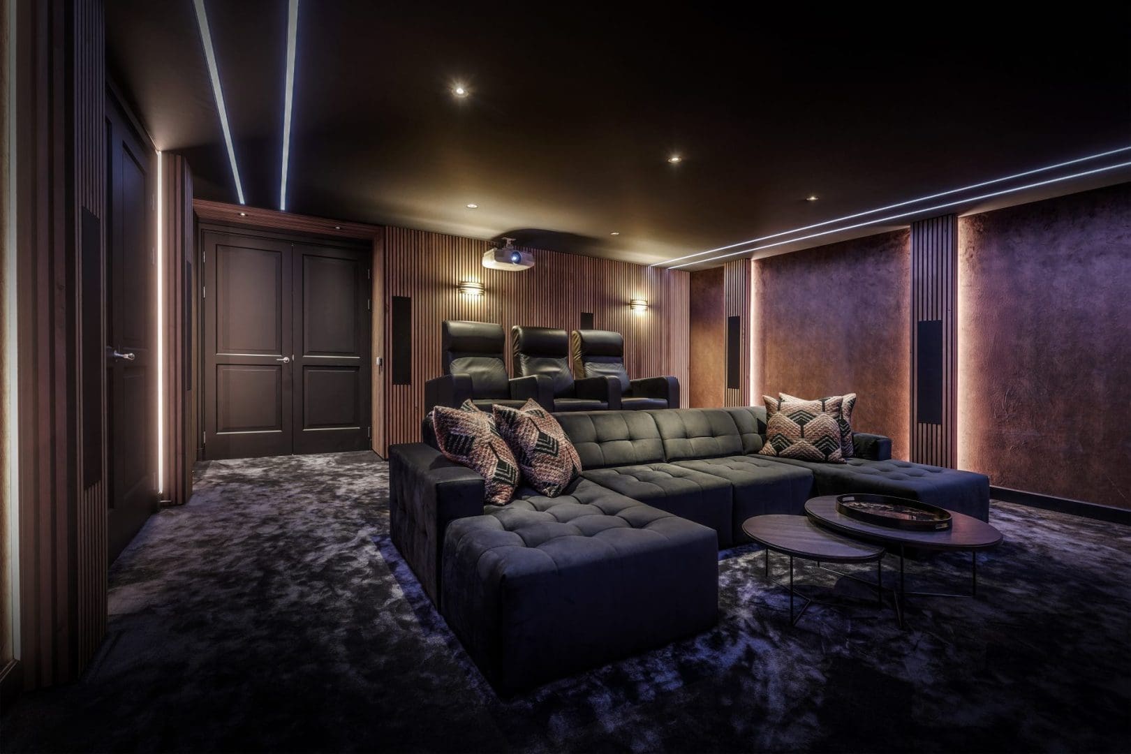 Luxe thuisbioscoop met een donkere hoekbank, drie fauteuils, houten wandpanelen en sfeervolle ledverlichting, Project Nova 0. Luxe thuisbioscoop met een donkere hoekbank, drie fauteuils, houten wandpanelen en sfeervolle ledverlichting, Project Nova 0.