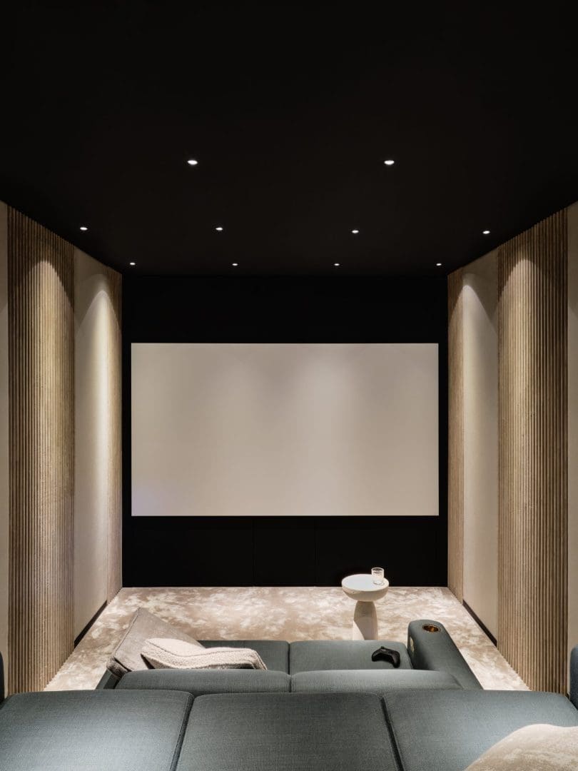 A modern home cinema with a large screen, gray sofas, wood paneling, and recessed spotlights in the black ceiling. A modern home cinema with a large screen, gray sofas, wood paneling, and recessed spotlights in the black ceiling.