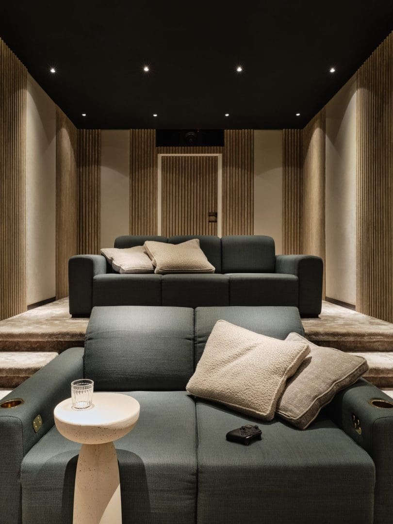Two gray sofas in a home cinema with wooden slatted walls, a black ceiling, and a small side table. Two gray sofas in a home cinema with wooden slatted walls, a black ceiling, and a small side table.