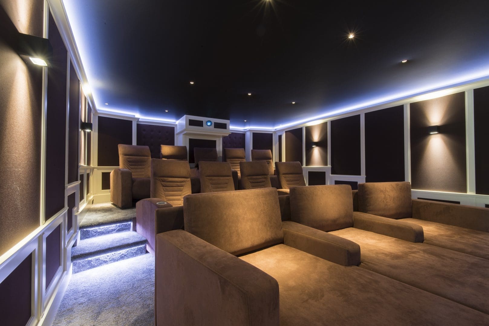 Luxe thuisbioscoop met bruine fauteuils, sfeervolle wandverlichting en een verlichte trap in een moderne ruimte.