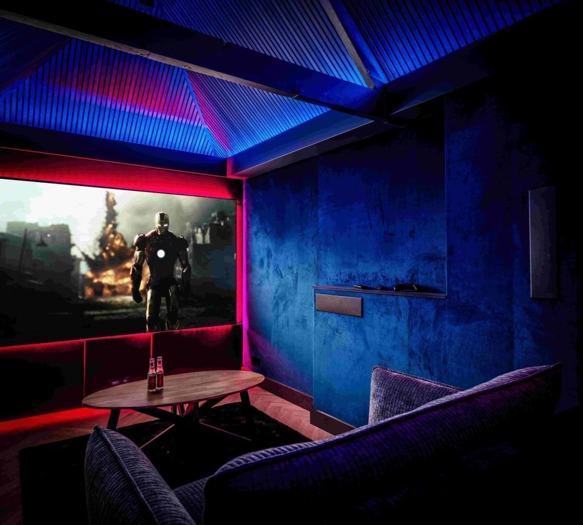 Een thuisbioscoop met een bank, een salontafel en een groot scherm waarop Iron Man te zien is, verlicht met blauwe accenten.