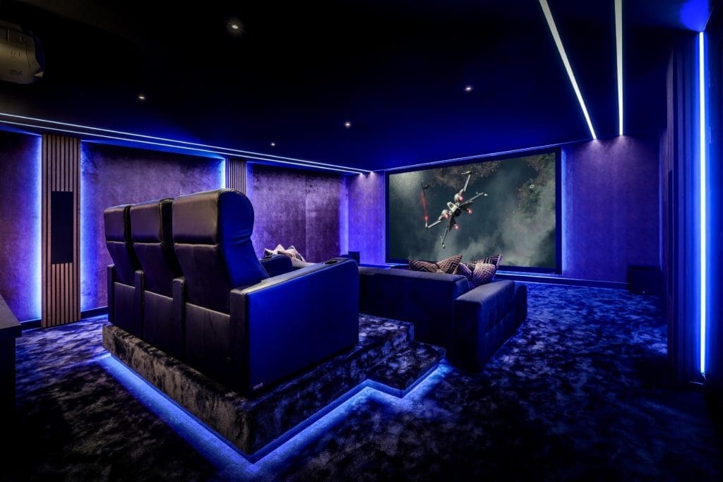 Luxe thuisbioscoop met zwarte fauteuils en blauwe ledverlichting, op het scherm is een ruimteschip uit Star Wars te zien. Luxe thuisbioscoop met zwarte fauteuils en blauwe ledverlichting, op het scherm is een ruimteschip uit Star Wars te zien.